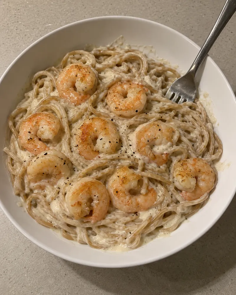 Plato de spaghetti integrales con salsa blanca cremosa de coliflor y gambas a la plancha por encima