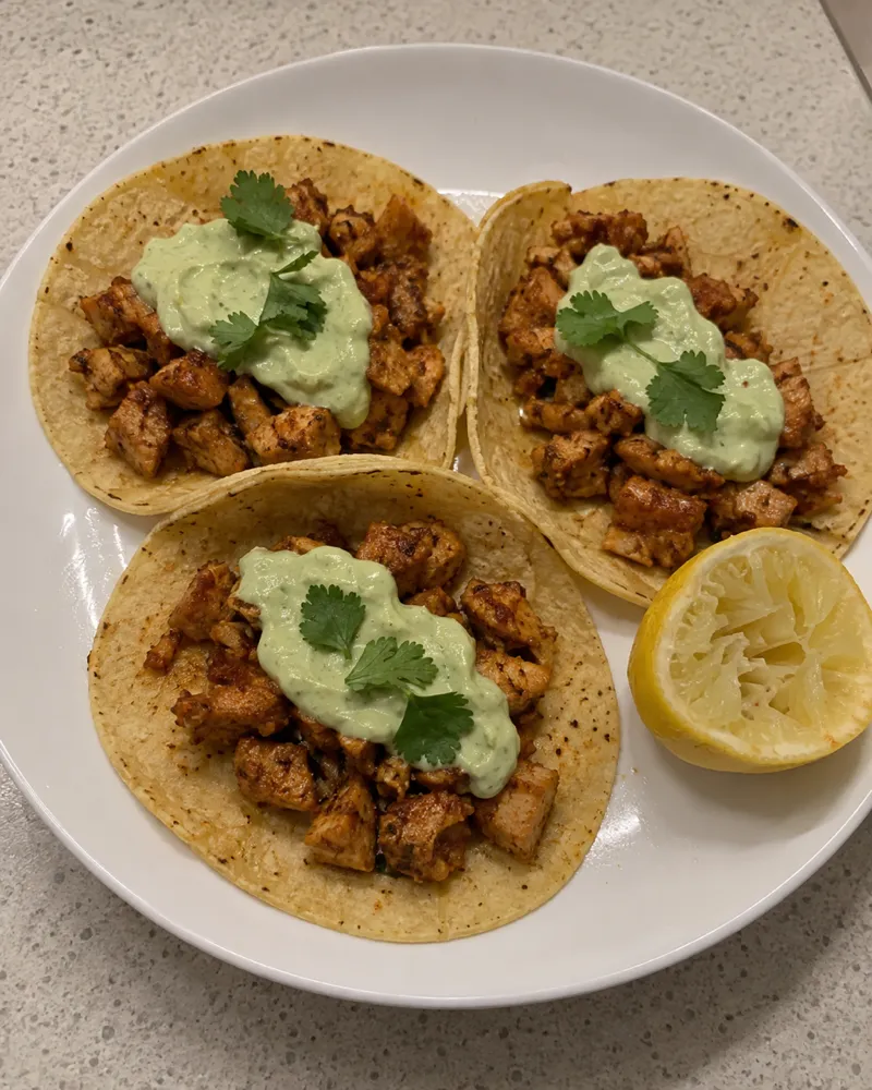Tres tortillas de maíz con tacos de pavo dorados con pimentón y una cucharada de crema verde de aguacate y yogur con hojas de cilantro