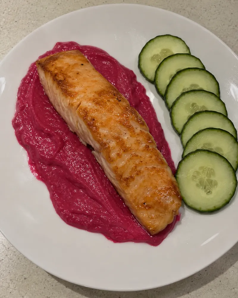Salmón a la plancha sobre una salsa rosa fucsia de remolacha y yogur, con rodajas de pepino al lado