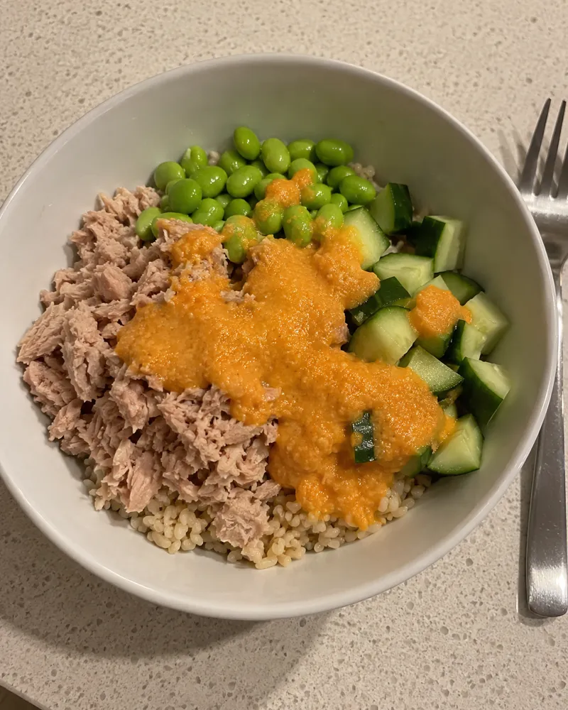 Bol de arroz integral con atún, edamame, pepino en dados y aliño naranja de zanahoria y jengibre por encima